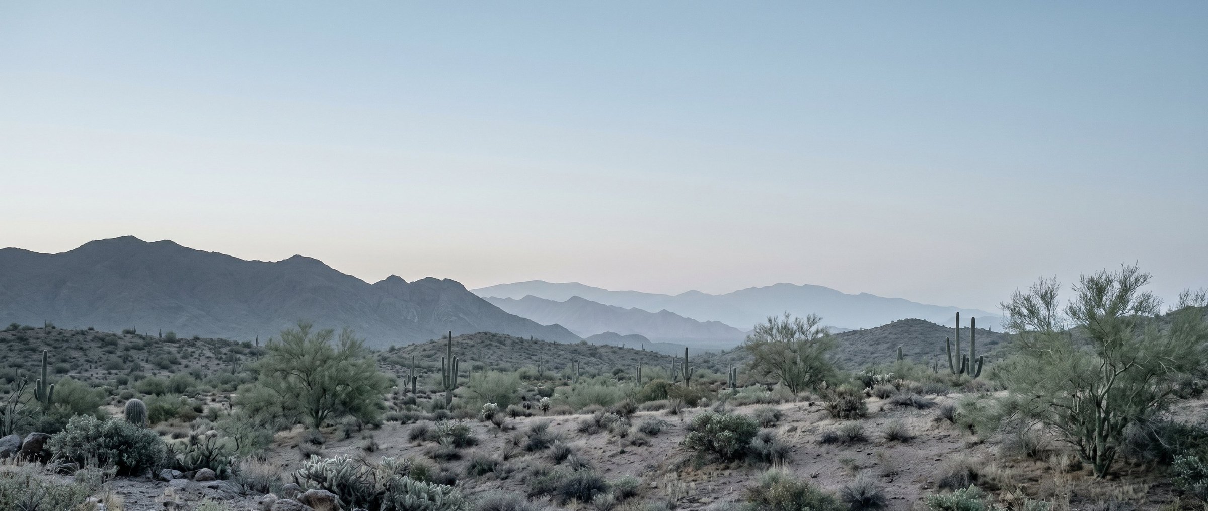A wide Sonoran Desert landscape at dawn with layered mountain ranges receding into the distance